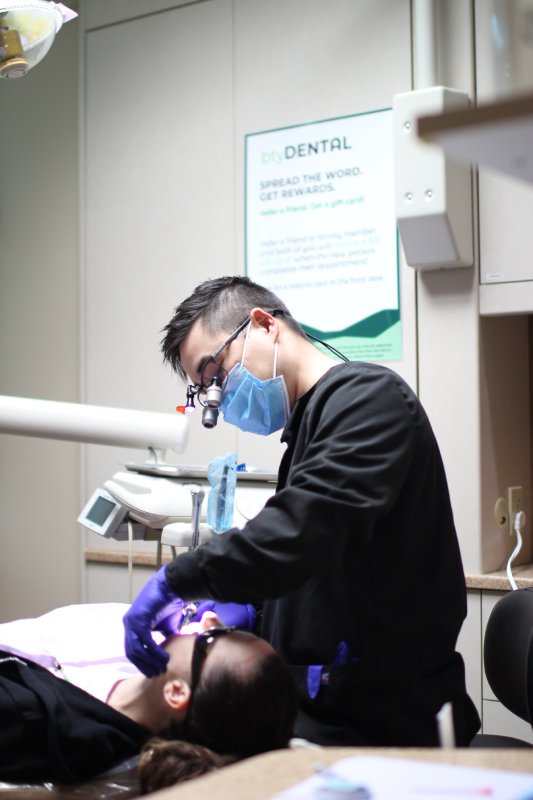 Dentist Performing Treatment - btyDENTAL A dentist wearing protective gear performs a dental procedure on a patient in the operatory, showcasing professional and attentive care - btyDENTAL