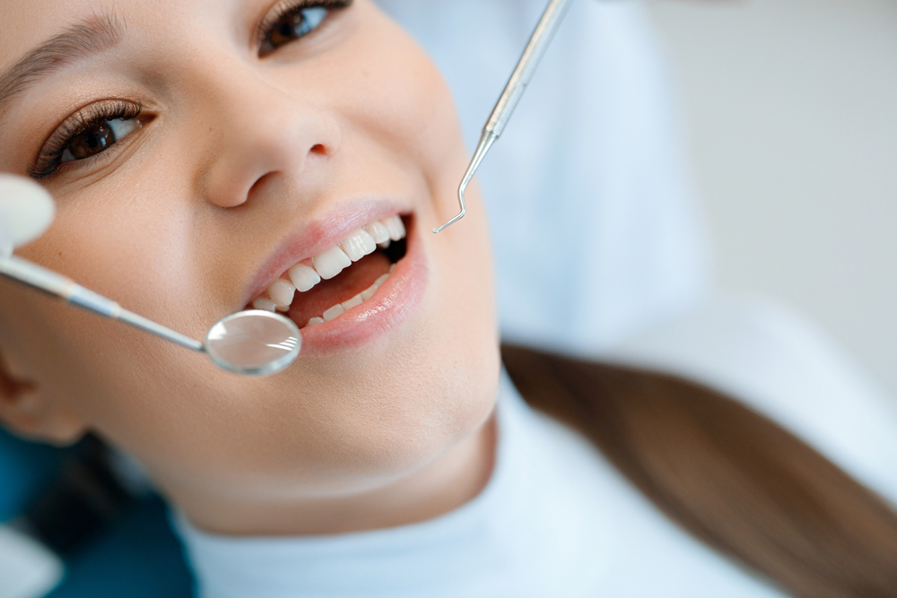 Dental exam with mirror and probe - Dentist in Lynnwood, WA Close-up of a young woman smiling during a routine dental checkup as the dentist uses a mirror and dental probe for examination - Dentist in Lynnwood, WA