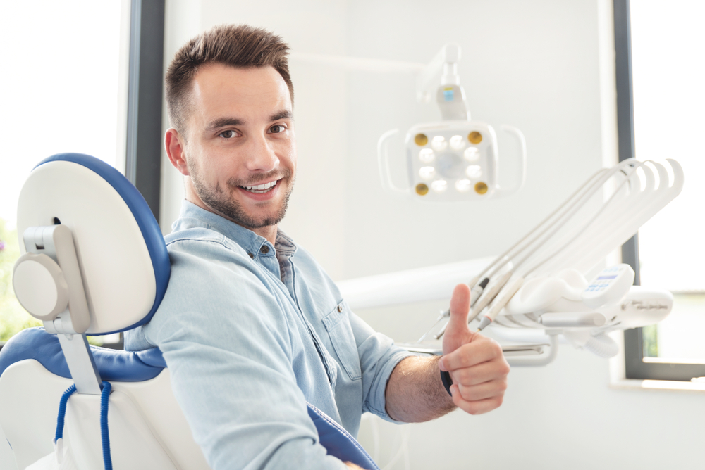 Handsome man showing thumbs up and smiling sitting at the dental chair - Veneers in Federal Way