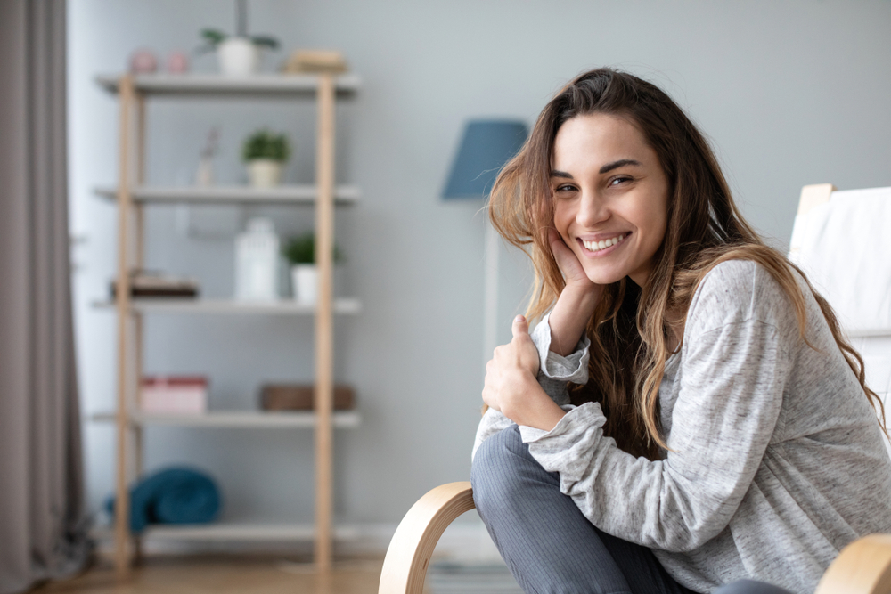 Young woman smiling happily at home - Emergency Dentist Sumner A cheerful young woman sitting comfortably indoors, smiling with confidence and warmth - Emergency Dentist Sumner