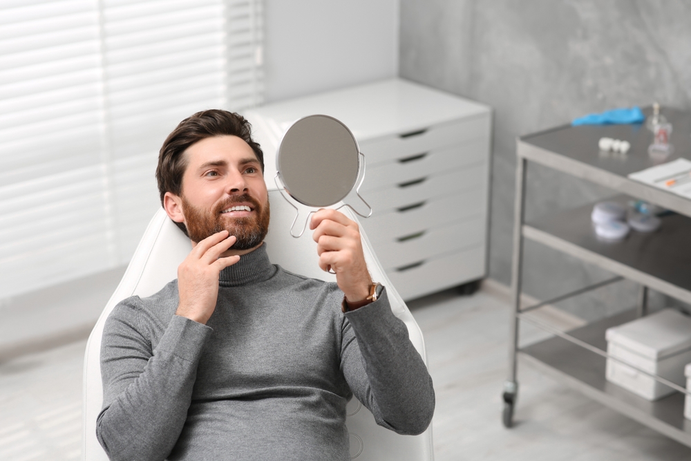 Patient checking smile after dental treatment - Dentist in Lynnwood, WA A man sitting in a dental chair smiling and examining his teeth in a mirror after treatment - Dentist in Lynnwood, WA