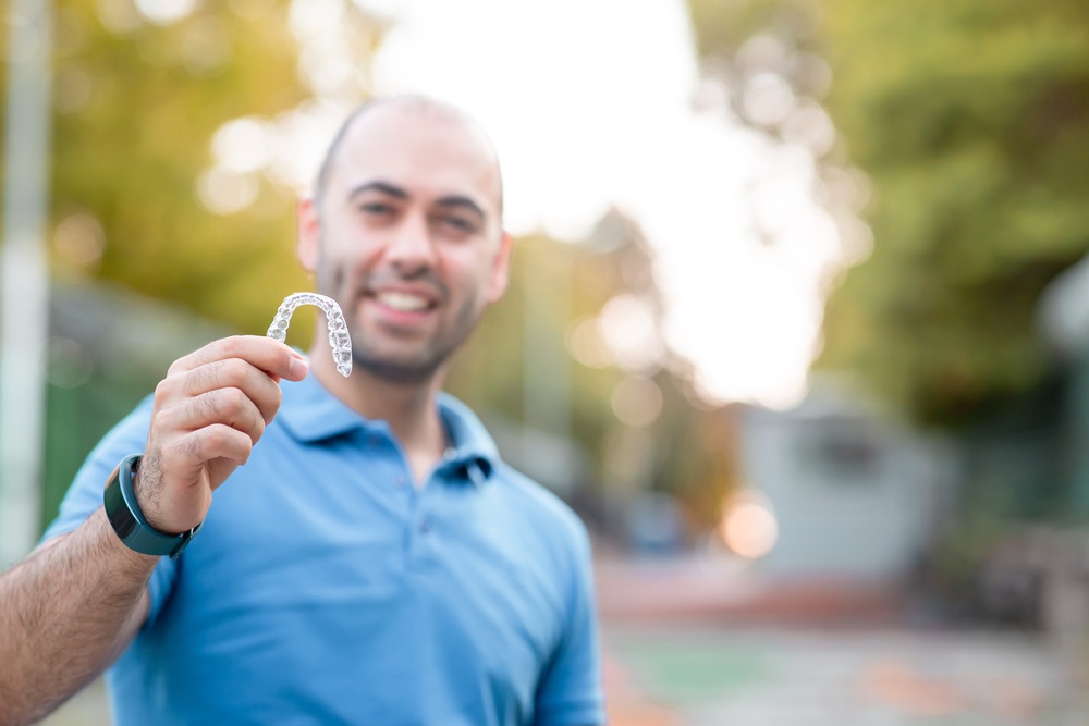 man with warm smiling is holding an invisaligner - Veneers in Lynnwood WA man with warm smiling is holding an invisaligner - Veneers in Lynnwood WA