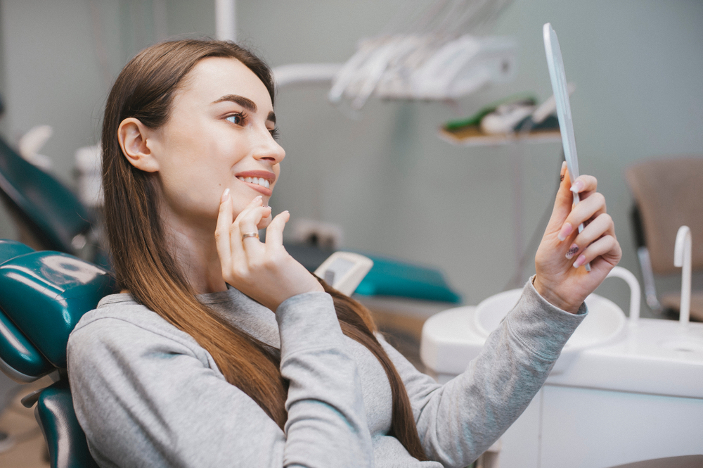 Patient checking smile after dental treatment - Dentist in Bonney Lake WA A young woman sitting in a dental chair and looking at her reflection in a mirror, admiring her improved smile - Dentist in Bonney Lake WA
