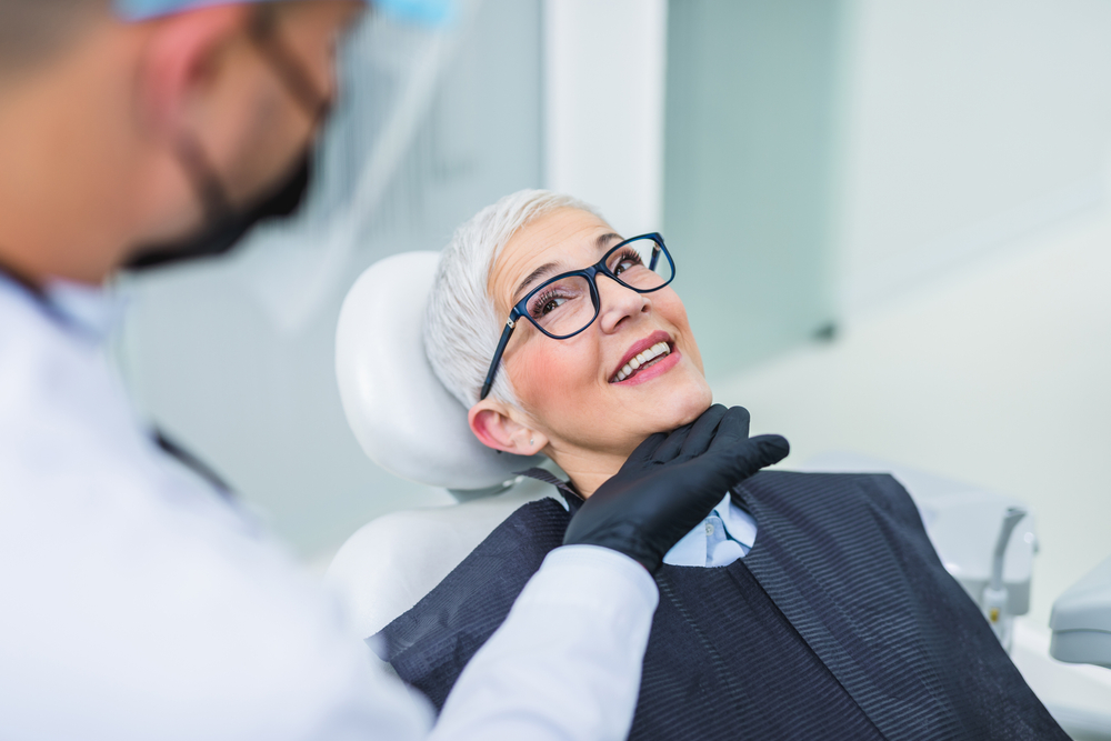 Senior woman consulting with dentist - Emergency Dentist Sumner A smiling senior woman in glasses sitting in a dental chair during a checkup with her dentist - Emergency Dentist Sumner