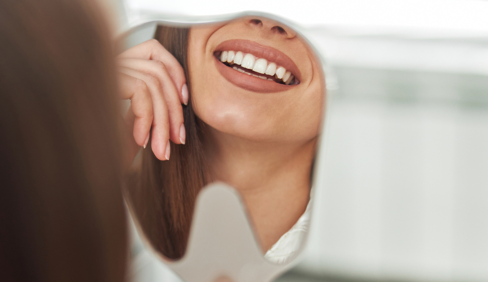 woman looking at teeth on the mirror with dental bridges woman looking at teeth on the mirror with dental bridges